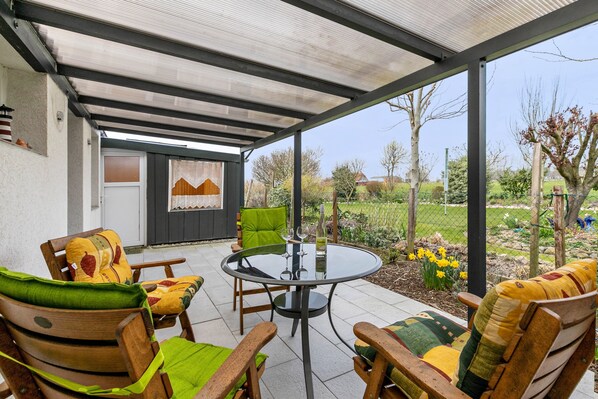An outdoor patio with a round table and chairs, a covered area, and a garden view.