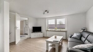 Una sala de estar moderna con un sofá, una mesa de centro, un televisor y una ventana con persianas.