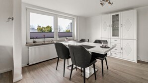 Una cocina moderna con encimera blanca, sillas negras y un armario blanco con puertas de vidrio.