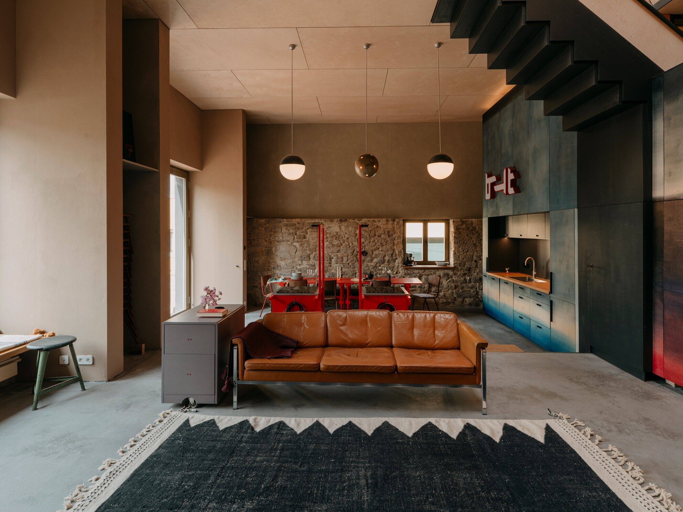 Ein modernes Wohnzimmer mit Ledersofa, Essbereich und einer Küche mit Steinwand.
