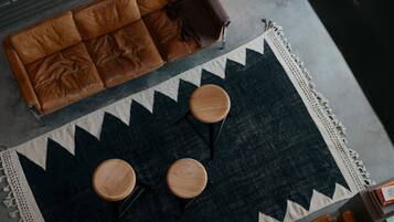 A brown leather sofa, two wooden stools, and a patterned rug in a room with a concrete floor and a metal grate.
