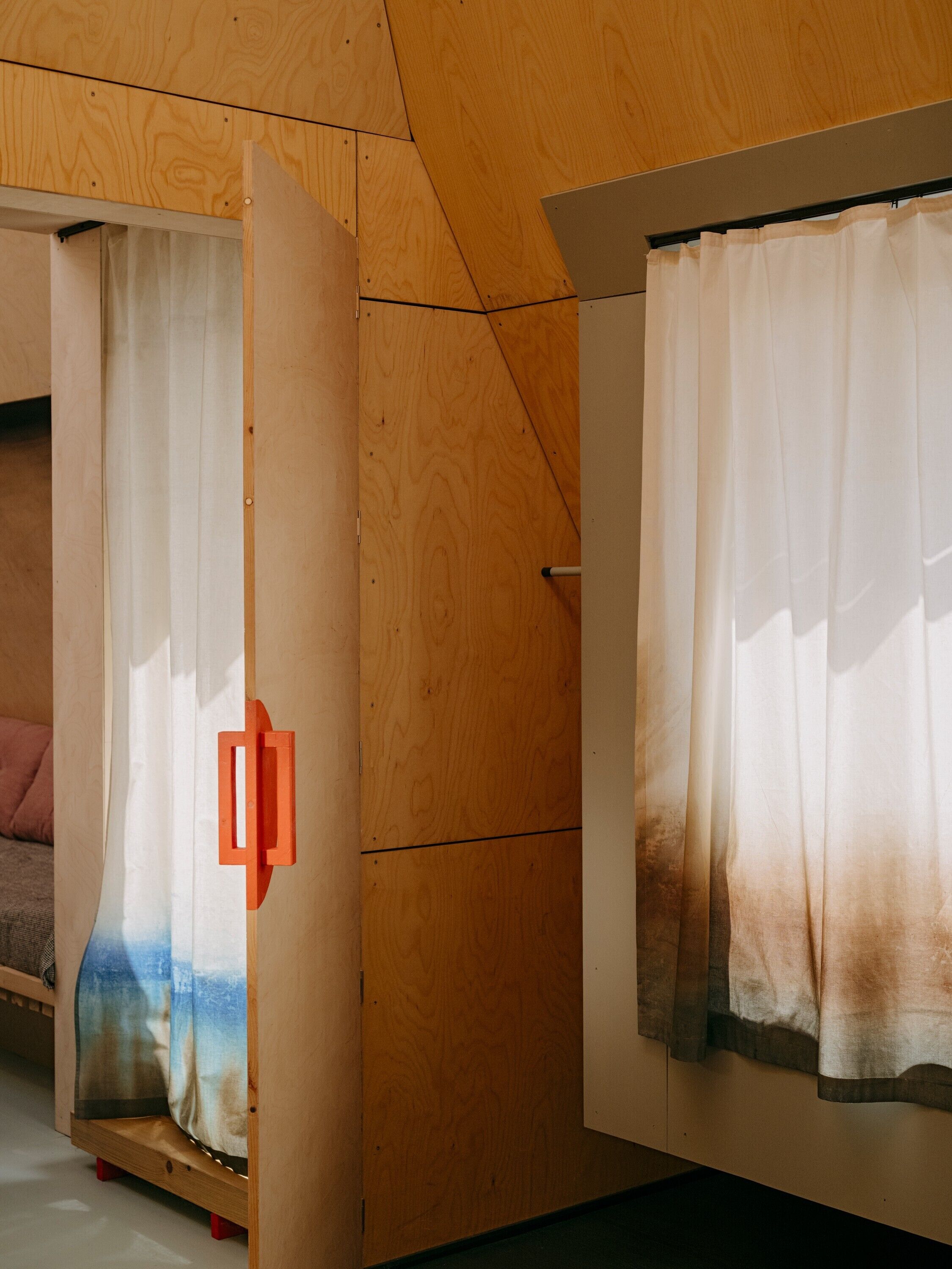 Una habitación con techo de madera, una cama con cabecera blanca y una ventana con cortina blanca.