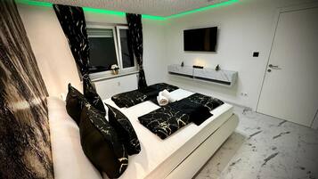 A modern bedroom with a bed, a TV, a shelf, and a door.