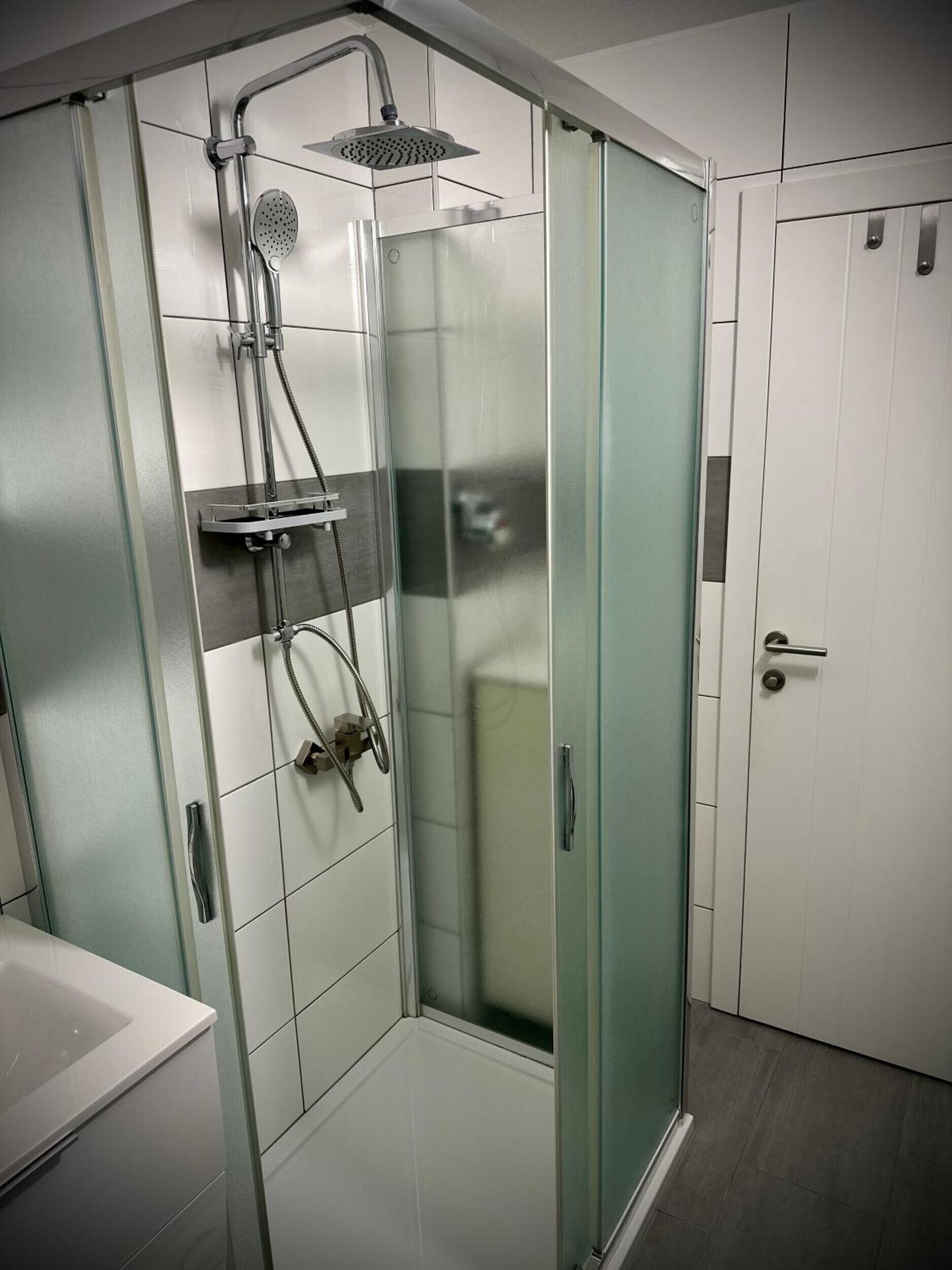 Un bany modern amb un compartiment de dutxa de vidre, un lavabo blanc i una porta amb mànec.