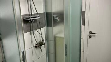 Un bany modern amb un compartiment de dutxa de vidre, un lavabo blanc i una porta amb mànec.