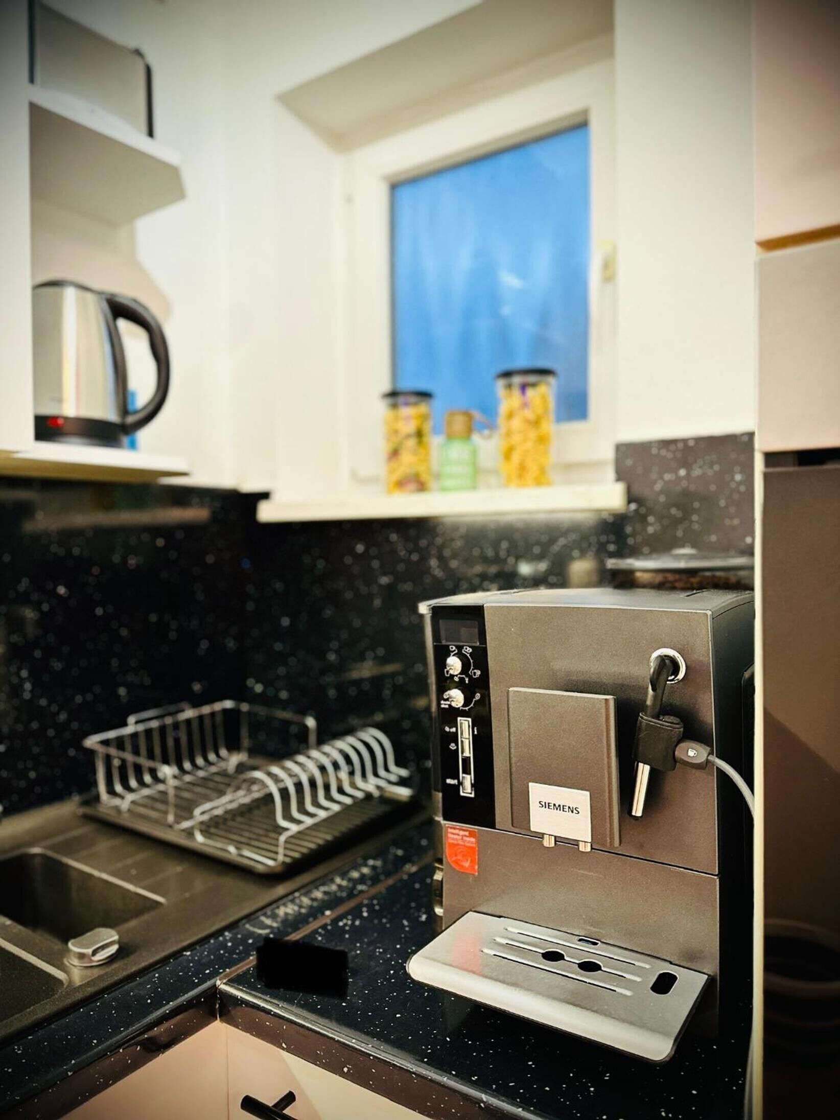Una cocina con cafetera, una ventana con vistas y un escurreplatos.