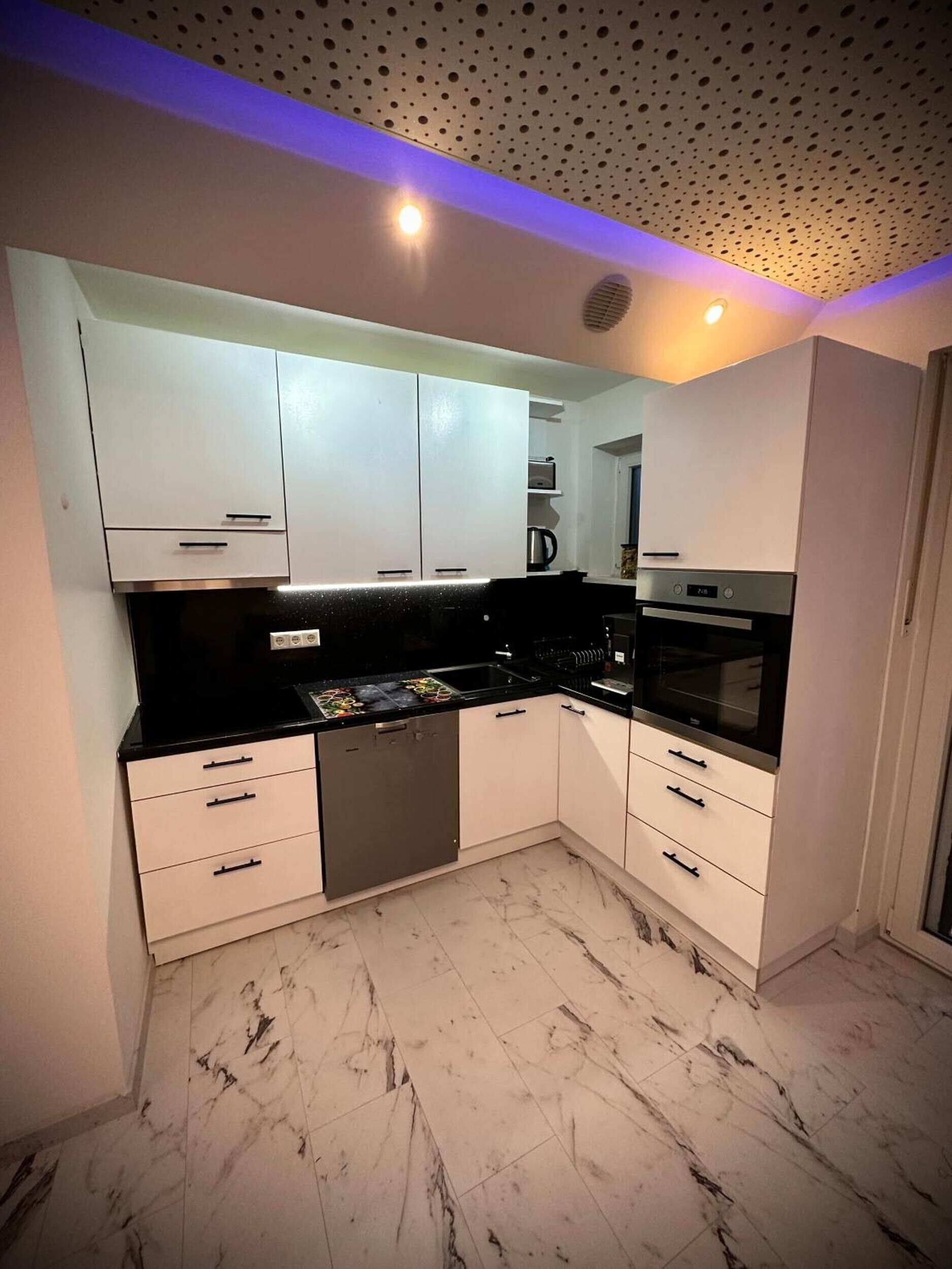 A modern kitchen with white cabinets, a black countertop, and a built-in oven.