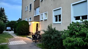 A multi-story building with a pathway leading to the entrance, a parked bicycle, and greenery around.