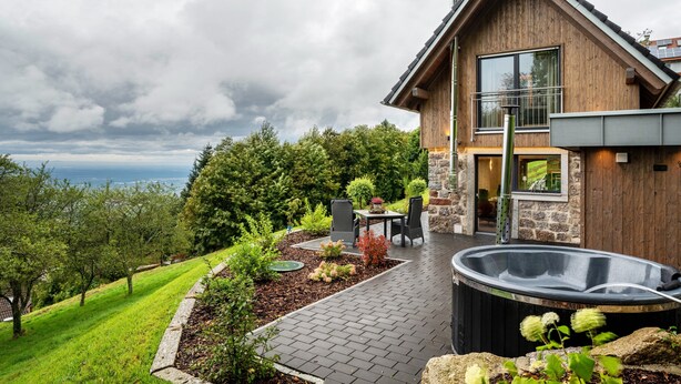 Une maison moderne avec une façade en pierre, un jacuzzi et une terrasse aménagée avec du mobilier d’extérieur.