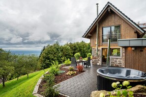 Une maison moderne avec une façade en pierre, un jacuzzi et une terrasse aménagée avec du mobilier d’extérieur.