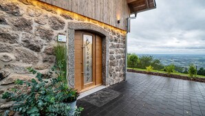Un bâtiment en pierre avec une porte en bois, une terrasse pavée et une vue sur le paysage.
