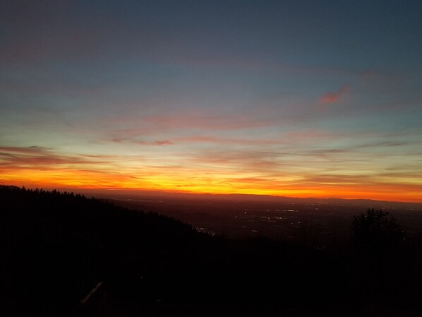 Un coucher de soleil sur une ville, avec la silhouette d’une colline au premier plan.