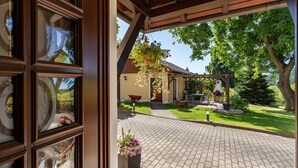 A covered patio area with a brick floor, a hanging flower basket, and a view of a house with a garden. - Apartment 'Ferienwohnung Am Augusttal' with Mountain View, Private Terrace and Wi-Fi (Hainewalde)