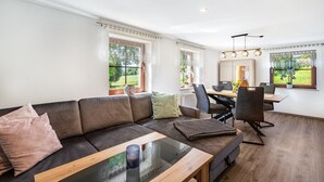 A modern living room with a sofa, a glass coffee table, and a dining area with chairs and a table. - Apartment 'Ferienwohnung Am Augusttal' with Mountain View, Private Terrace and Wi-Fi (Hainewalde)