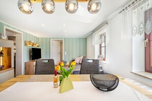 A dining area with a table, chairs, a vase with flowers, and a television in the background.