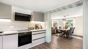 A modern kitchen with built-in appliances, a dining area with a table and chairs, and a view of the outdoors. - Apartment 'Ferienwohnung Am Augusttal' with Mountain View, Private Terrace and Wi-Fi (Hainewalde)