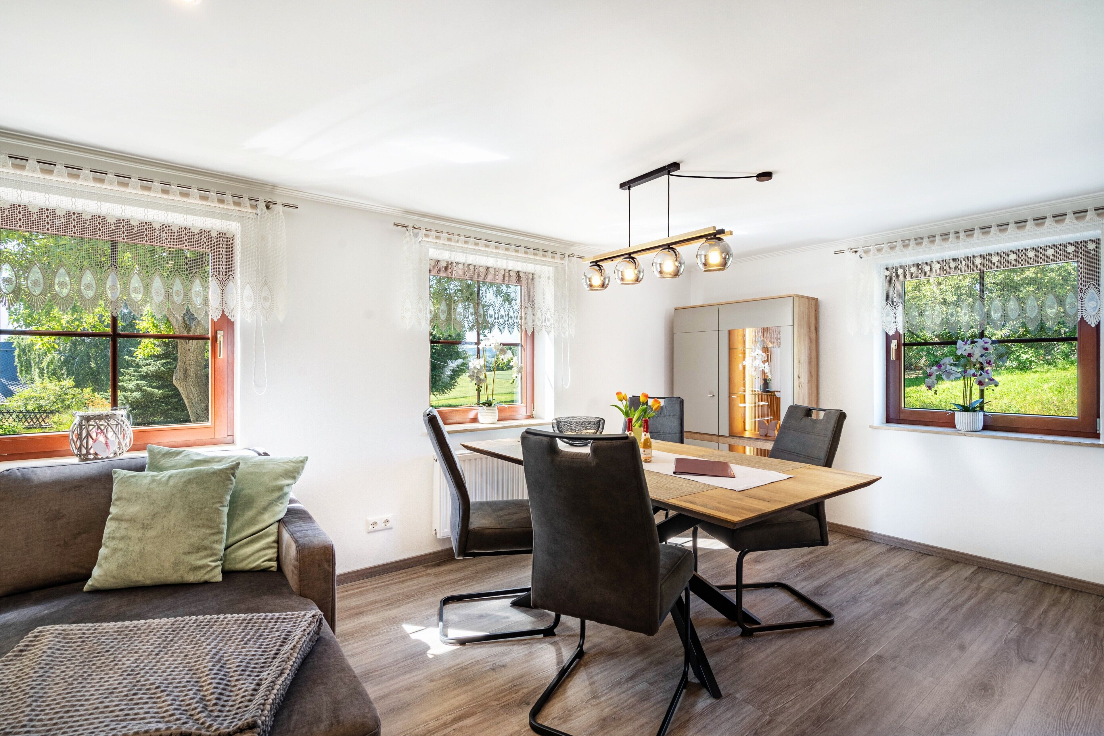 A modern dining area with a wooden table, black chairs, and a chandelier.
