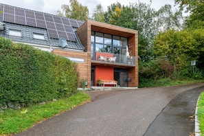 A modern house with solar panels, a balcony with outdoor furniture, and a well-maintained garden.