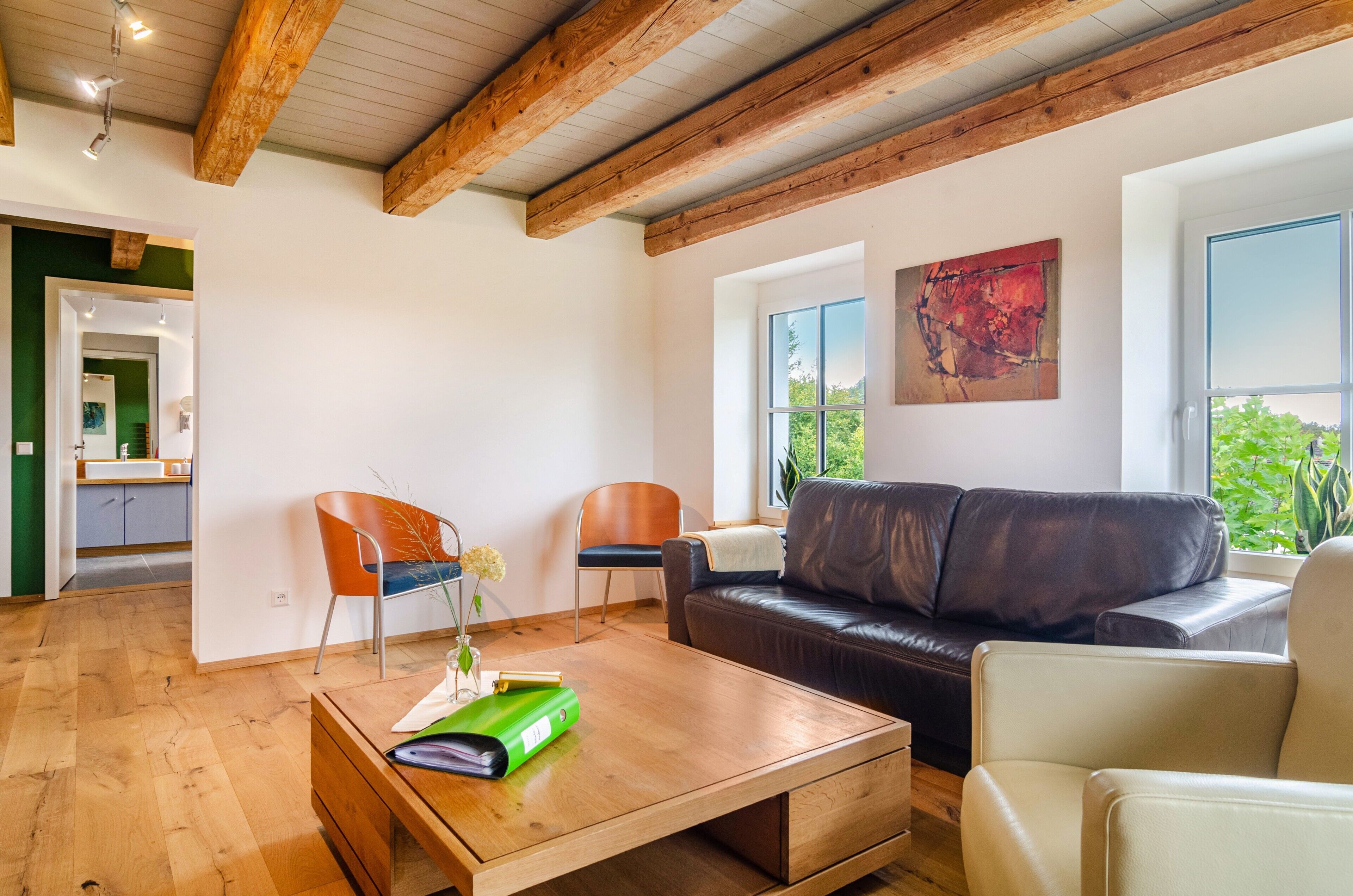 Un salon avec une table basse en bois, deux fauteuils, un canapé et un tableau accroché au mur.