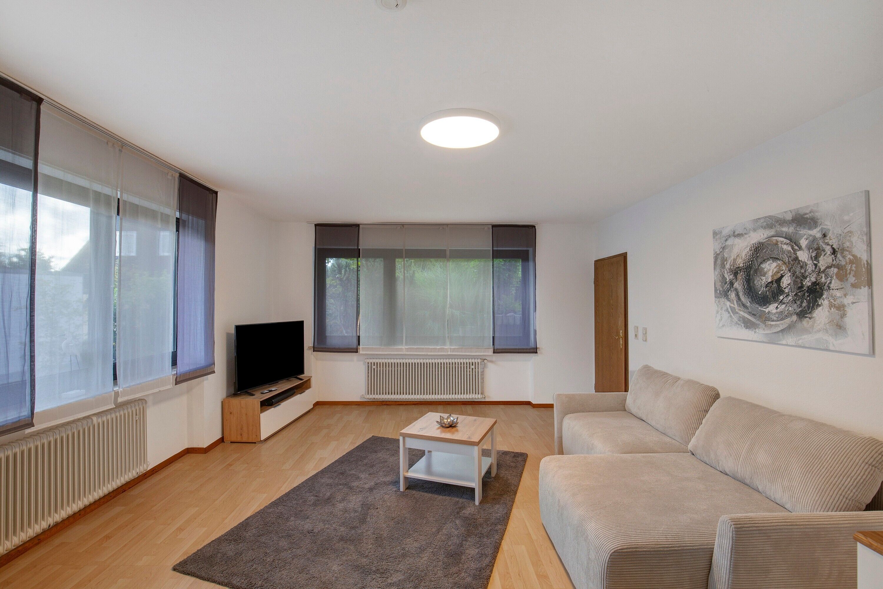 Una sala de estar con sofá, mesa de centro, televisor y ventanas amplias.
