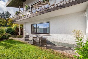 Ein modernes Haus mit Balkon, einer Terrasse und Gartenmöbeln sowie einem Garten.