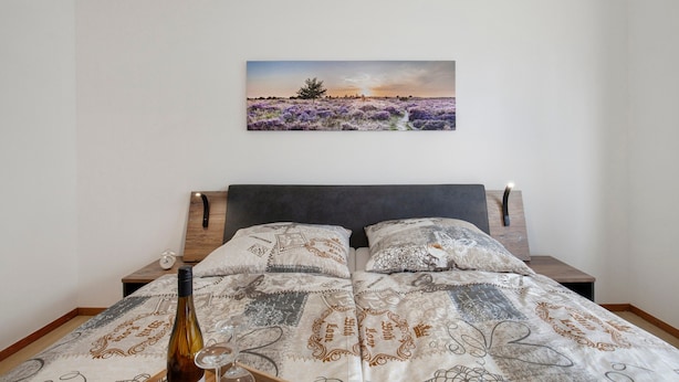 Ein Schlafzimmer mit einem Bett, einem Nachttisch, einer Flasche und einem Glas.