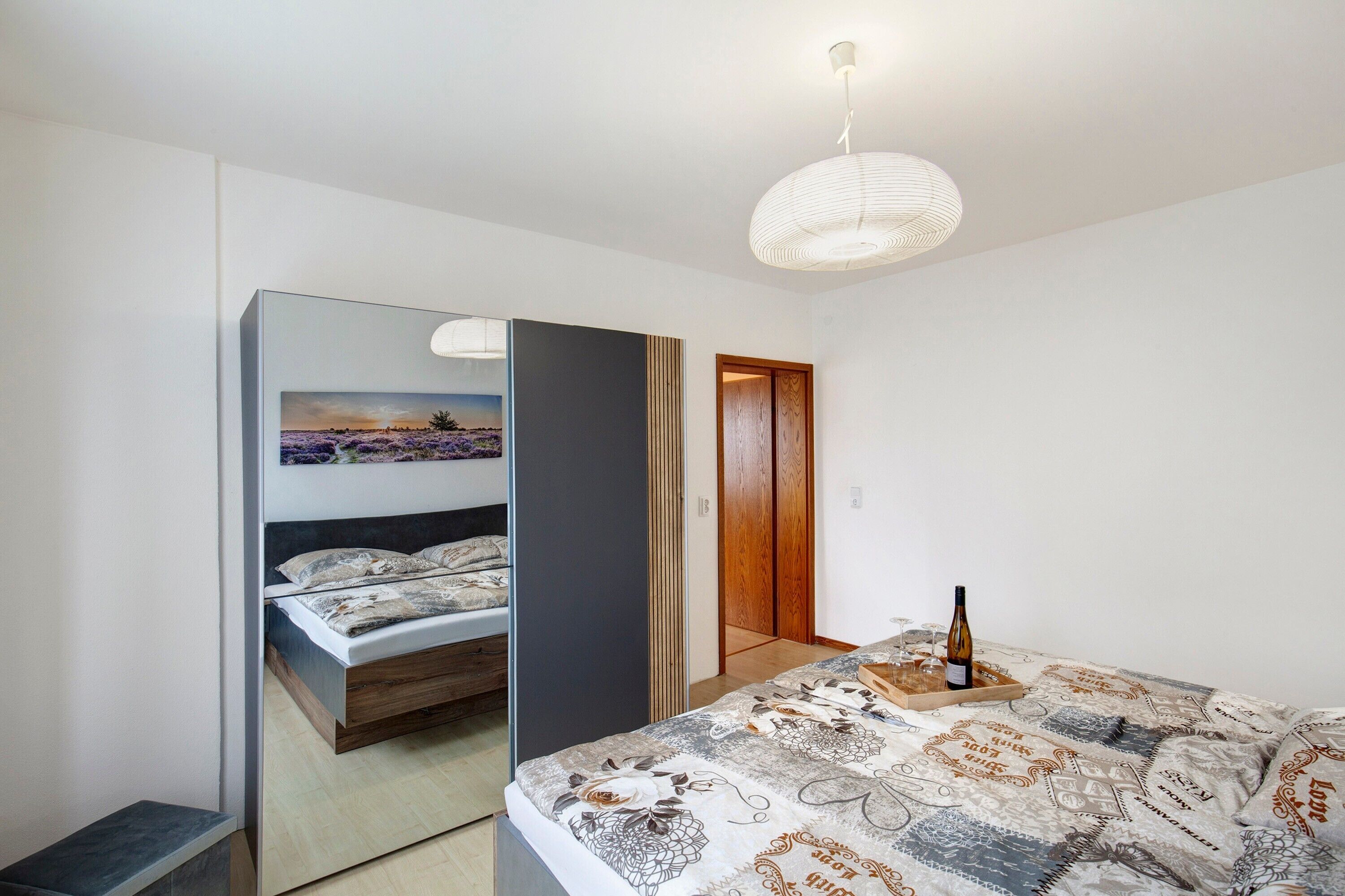 A bedroom with a bed, a mirror, a wooden door, and a bottle on the bed.