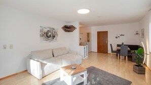 Ein Wohnzimmer mit einer Couch, einem Couchtisch, einem Essbereich mit Stühlen, einem Schrank und einer Tür.