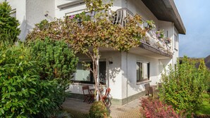 Ein zweistöckiges Haus mit einer Laube, einem kleinen Garten und einer sichtbaren Tür.