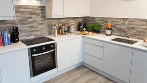 A modern kitchen with white cabinets, a stainless steel range hood, a built-in oven, a sink, and a clock on the wall.