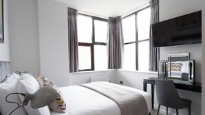 Una habitación de hotel moderna con una cama grande, un escritorio con computadora y televisión.