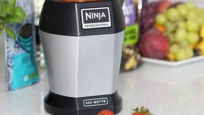 A Ninja Professional blender with 900 watts, filled with orange juice, on a kitchen counter with fruits and a plant nearby.