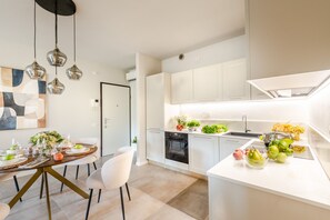 A modern kitchen with white cabinets, a built-in oven, and a dining area with a round table and chairs. - Casa Prospero in Lucca (Lucca)