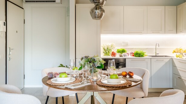Una cocina moderna con armarios blancos, una mesa de comedor con platos, vasos y un florero.