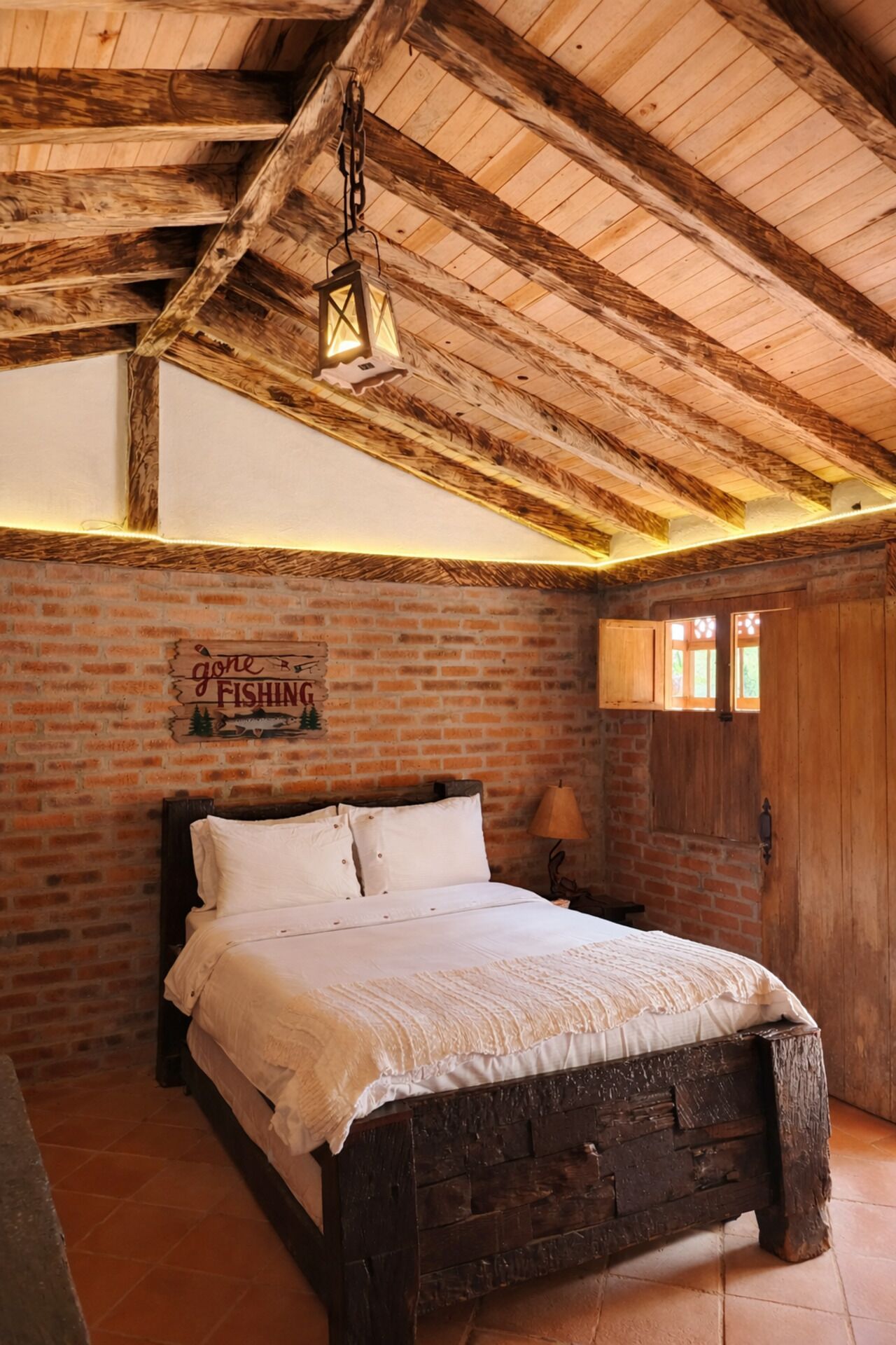 Un dormitorio rústico con cama de madera, paredes de ladrillo y una lámpara colgante.