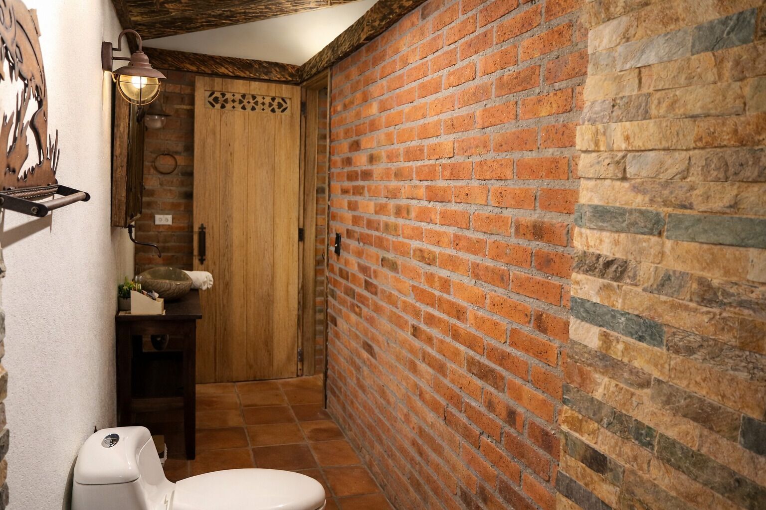 Un baño con inodoro blanco, puerta de madera y pared de ladrillo.