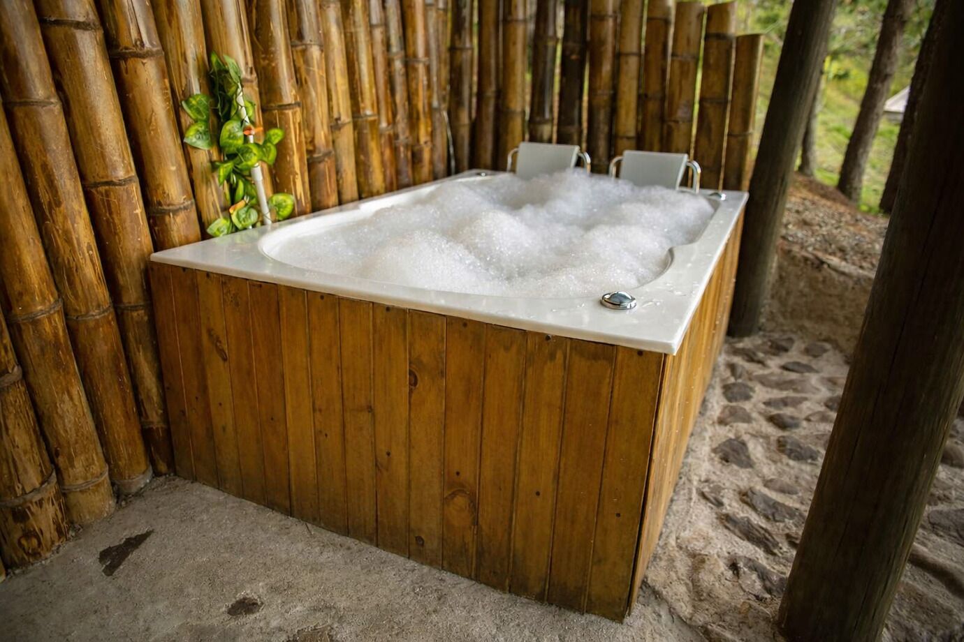 A wooden hot tub with a white interior, surrounded by bamboo walls and a sandy ground.