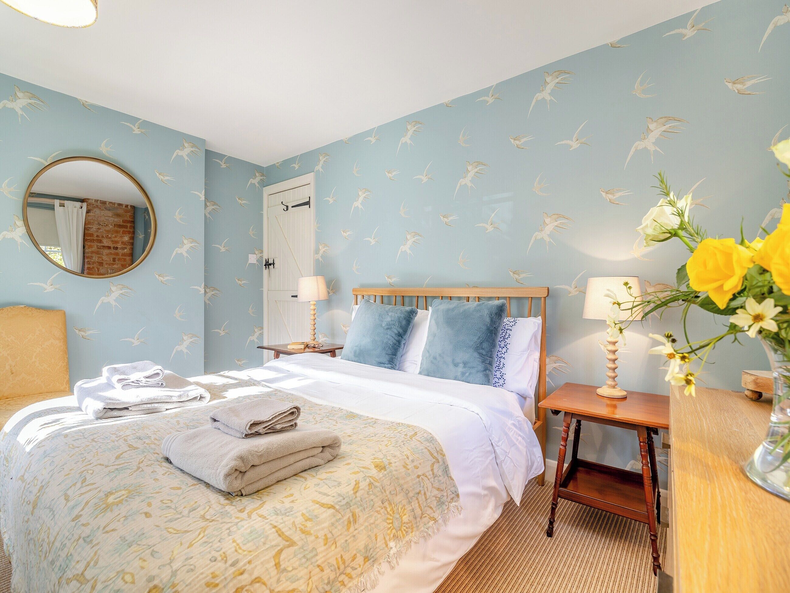 A bedroom with a bed, a nightstand, a mirror, a dresser, and a vase with flowers.