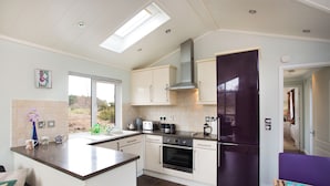 A modern kitchen with a central island, built-in oven, and a large refrigerator. - Bluebell Lodge - Sleeps 4,hot Tub, Loch & Woodland (Strathpeffer)