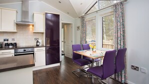 A modern kitchen with white cabinets, a stainless steel range hood, and a wooden dining table with purple chairs. - Bluebell Lodge - Sleeps 4,hot Tub, Loch & Woodland (Strathpeffer)
