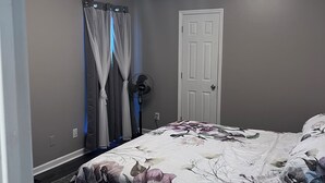 Un dormitorio con cama, lámpara en el techo, una puerta y una ventana con cortinas.