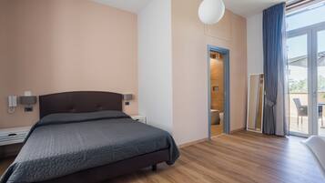 A modern bedroom with a large bed, bedside tables, a wall-mounted lamp, and a sliding glass door leading to a balcony.