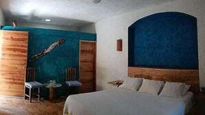 Een slaapkamer met een bed, twee stoelen, een klein tafeltje en een houten kledingkast.