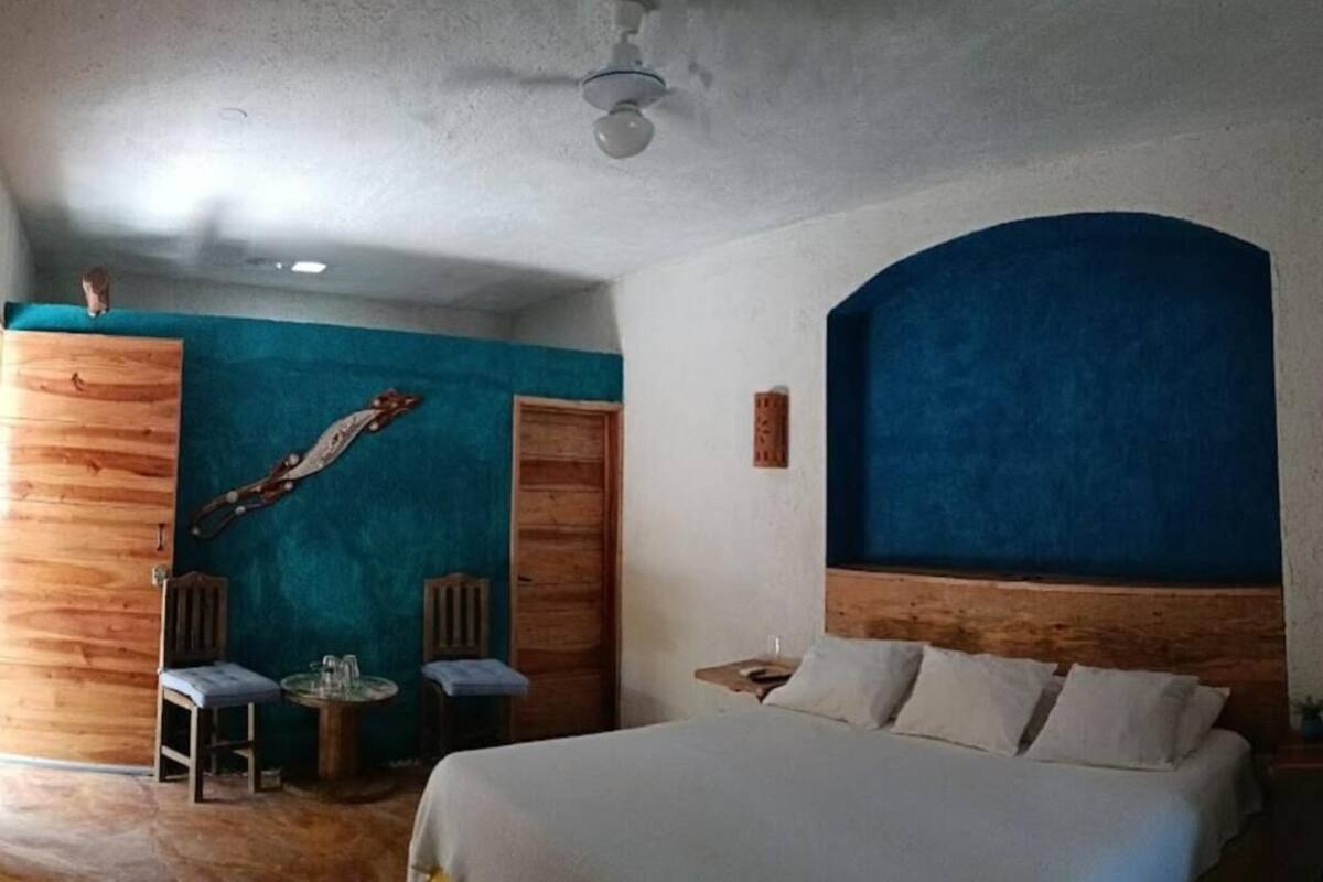 A bedroom with a bed, two chairs, a small table, and a wooden wardrobe.