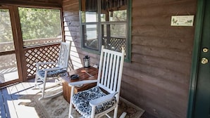 A wooden cabin with a porch featuring two white rocking chairs and a table.