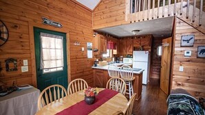 A cozy cabin interior with a dining area, kitchen, and a staircase leading to an upper level.