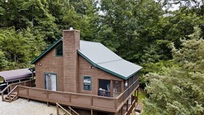 A wooden cabin with a green roof, a balcony, and a staircase leading to the entrance.