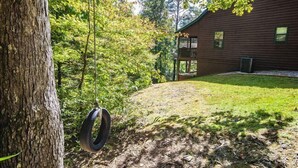 A wooden cabin with a porch, surrounded by trees and a grassy yard.