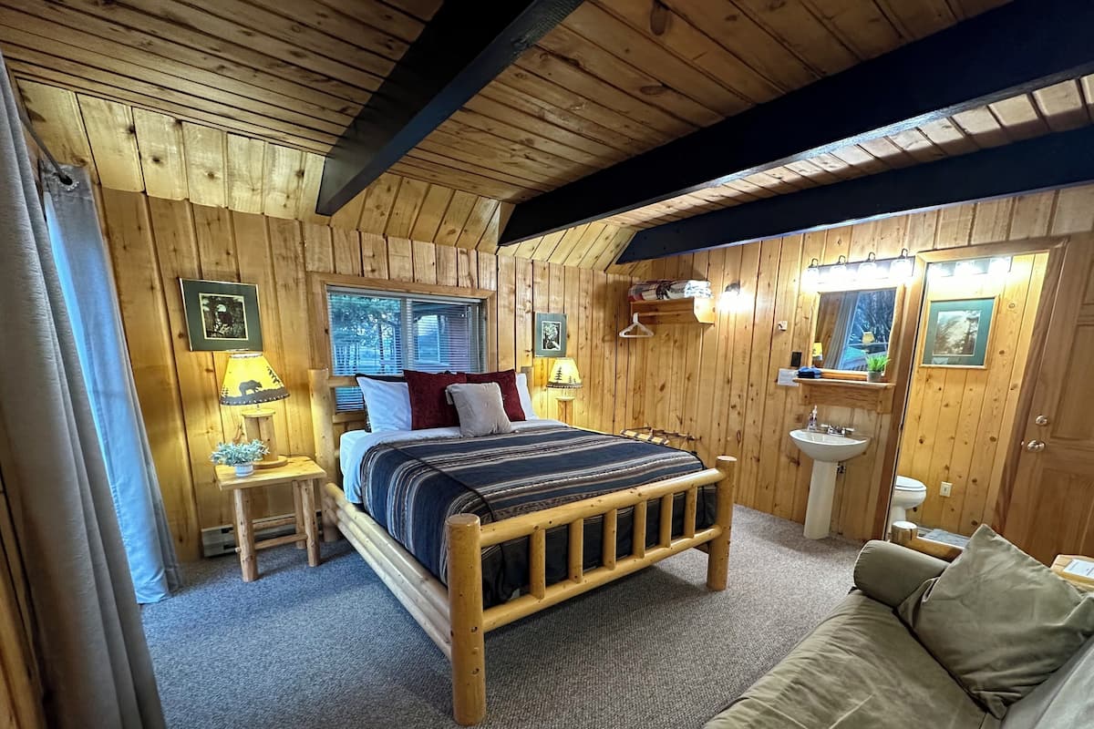 A wooden cabin bedroom with a bed, bedside tables, a mirror, and a bathroom with a sink and toilet.