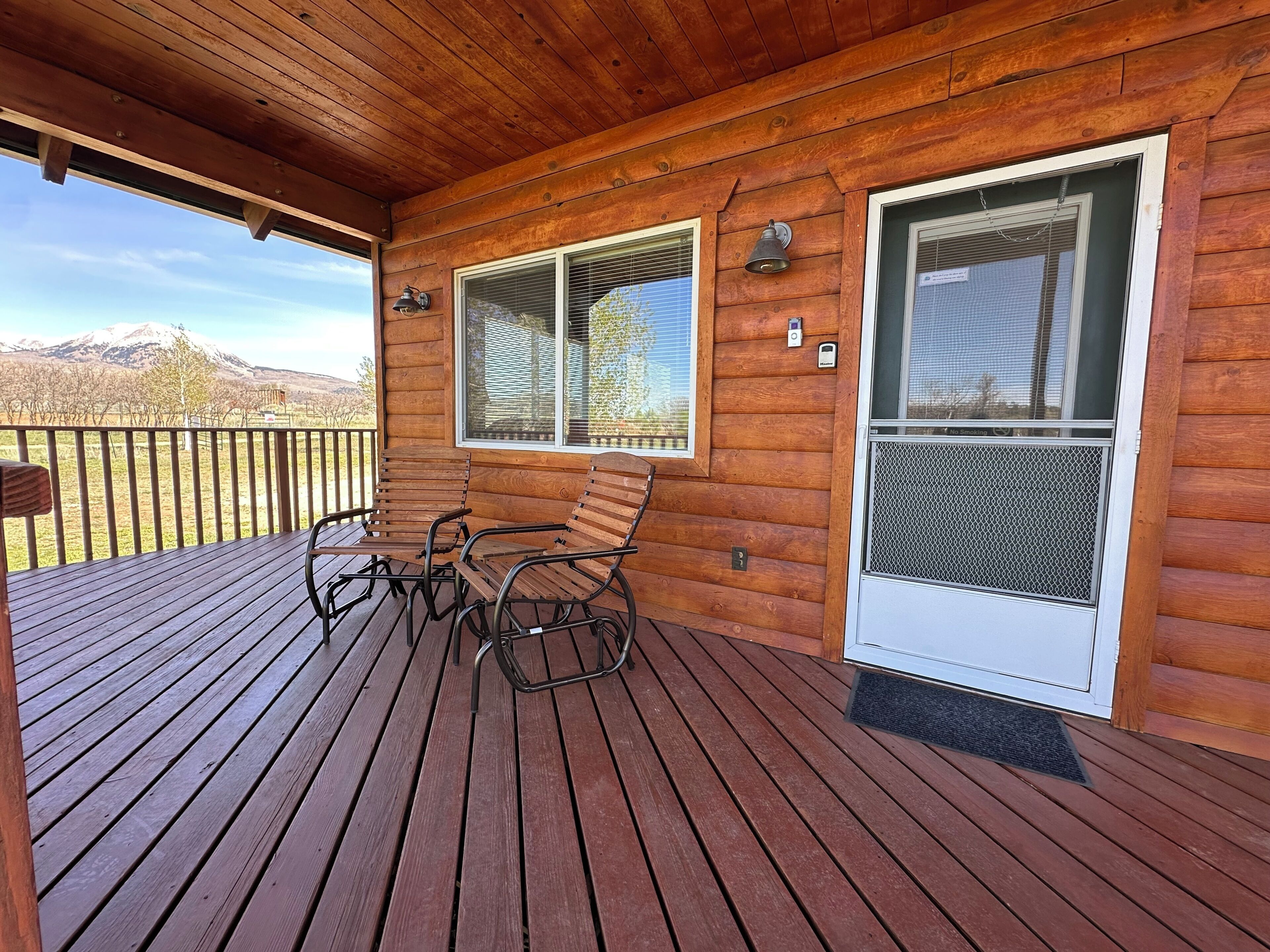 A wooden deck with two rocking chairs and a window with a mesh screen.